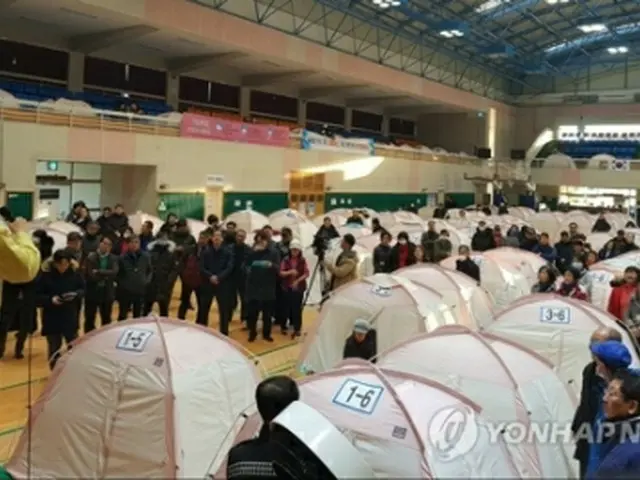 昨年１１月の地震により室内体育館で避難生活をしている市民も今回の余震に不安を募らせた。マイクで状況を説明する浦項市長＝１１日、浦項（聯合ニュース）