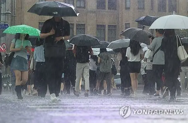 激しい雨が降る中、ソウル中心部の光化門広場付近を歩く人々＝１７日、ソウル（聯合ニュース）