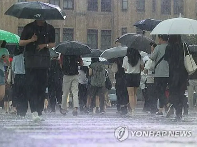 激しい雨が降る中、ソウル中心部の光化門広場付近を歩く人々＝１７日、ソウル（聯合ニュース）