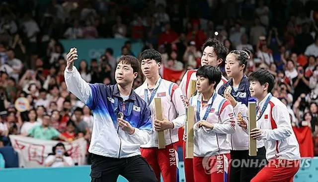 卓球混合ダブルスの表彰台で韓国選手（左端）の自撮りに応じる北朝鮮ペア（中央）と中国ペア＝７月３０日、パリ（聯合ニュース）