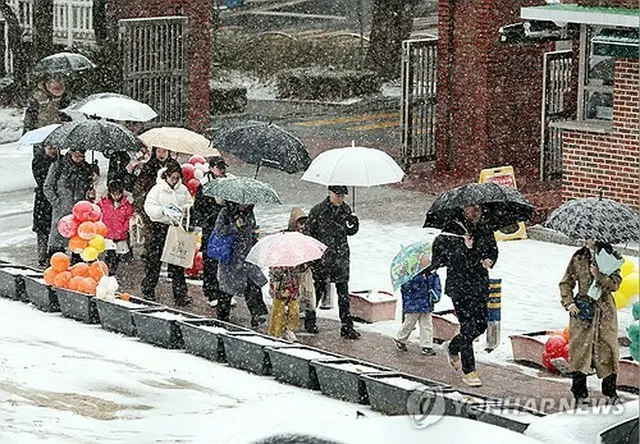 雪の中、傘を差してソウル市内の小学校で行われる入学式に参加する児童と保護者＝４日、ソウル（聯合ニュース）